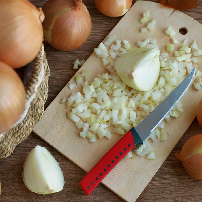 Onion whole and sliced. A lot of onions in a wicker basket. Sliced onions on a cutting board. Knife for cutting onions. Preparation of dishes from onions. vegetables for a healthy diet.