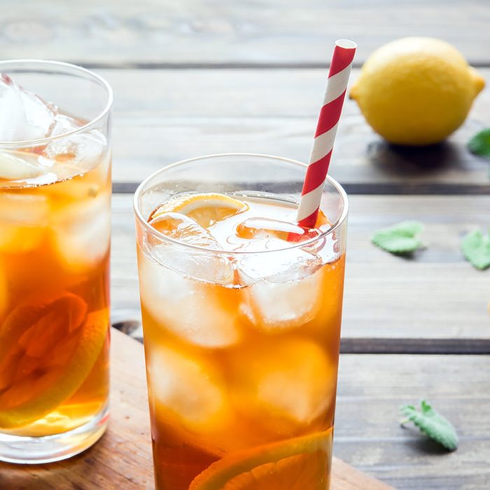 Iced tea with lemon slices, mint and ice cubes on wooden rustic background close up.