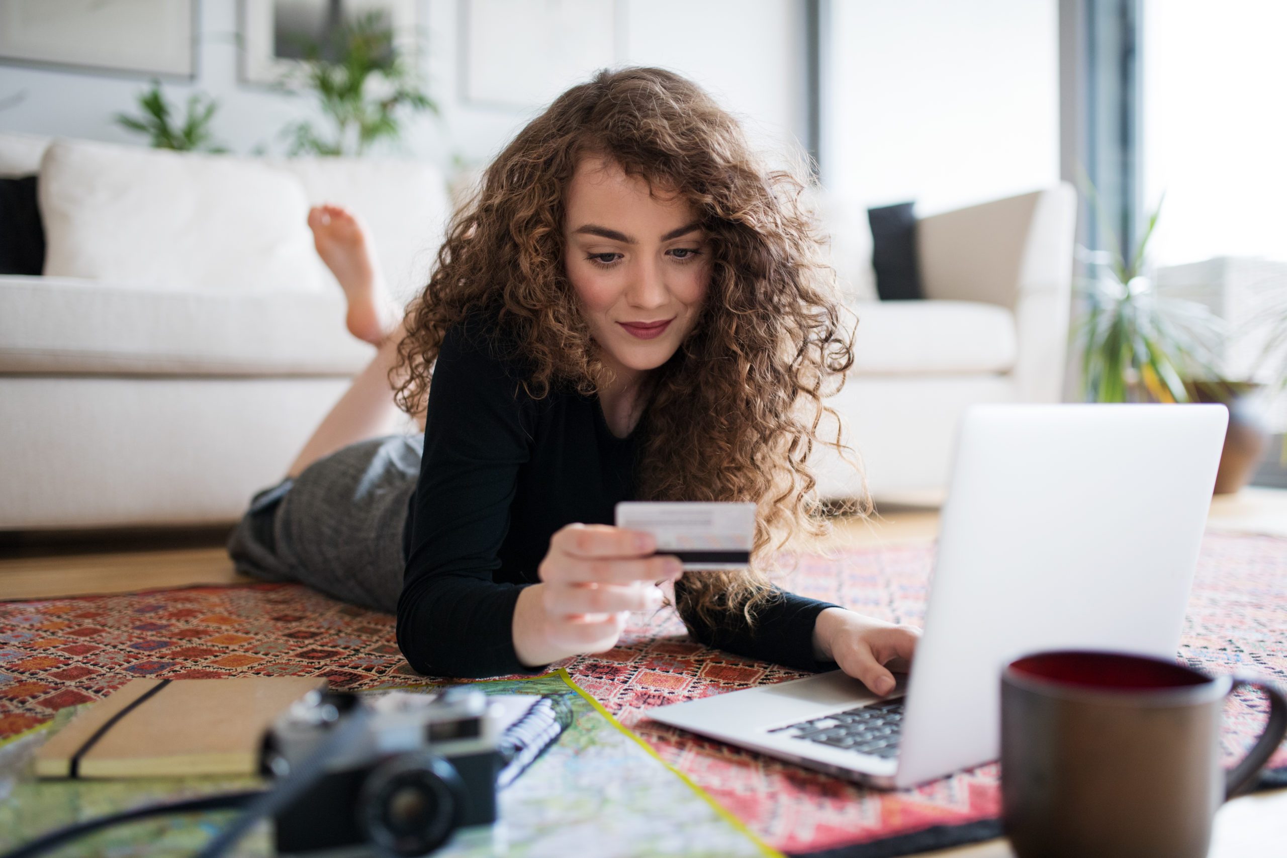 A young teenage girl with laptop, camera and map holding a card, making online payment.