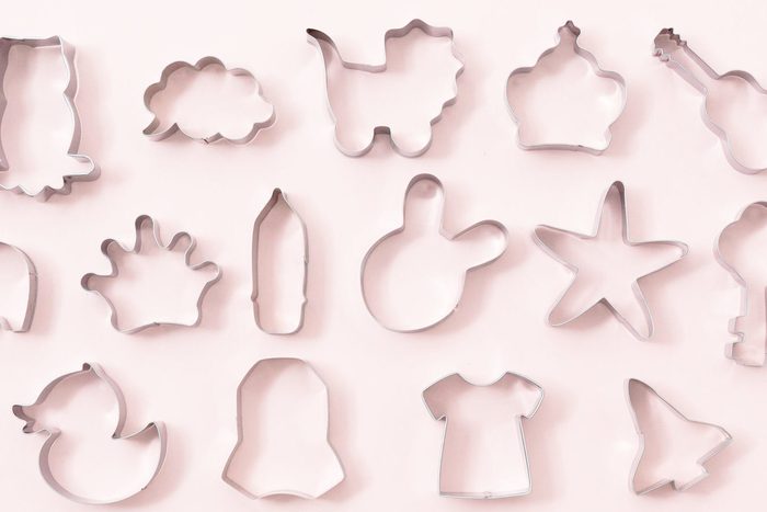 Cookies figures different shapes, top view, flat lay. Festive cookie cutters over white pink background. Tin biscuit cutters, tool to cut cookie dough. Figures for Easter, Christmas, child birthday