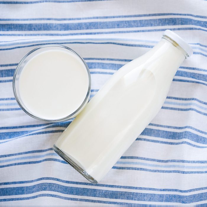 On a striped linen towel - filled glass and a glass bottle with fresh milk, close-up. The concept of healthy organic, farm food. Copy space for text
