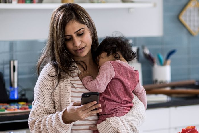 Mother holding baby and multi-tasking (texting) in kitchen