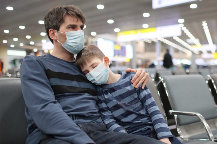 father putting medical mask on his son to protect himself from the coronavirus in an airport terminal or shopping mall