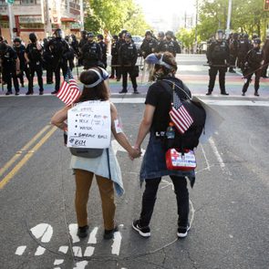 rear view shot of two protestors holding hands, american flags, and first aid kits
