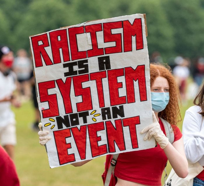 Protester holding a placard saying, Racism is a system not...