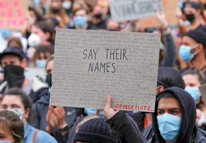 A protester wearing a face mask holds a placard saying say...