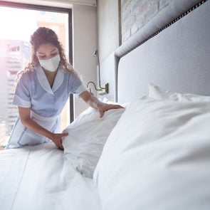Maid working at a hotel and doing the bed wearing a facemask