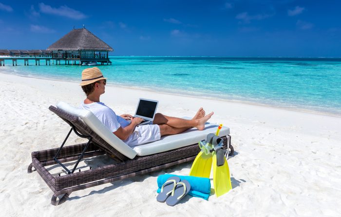 Traveler man sits on a tropical beach with his laptop and works