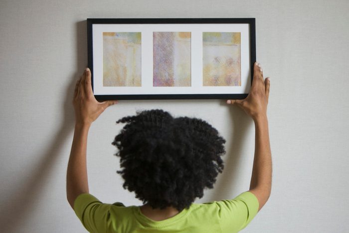 Mixed race woman hanging picture on wall