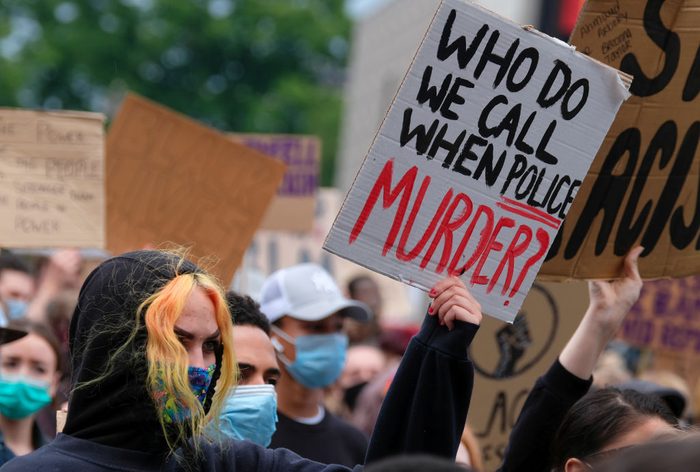 A protester holds a placard saying 'Who Do We Call When...