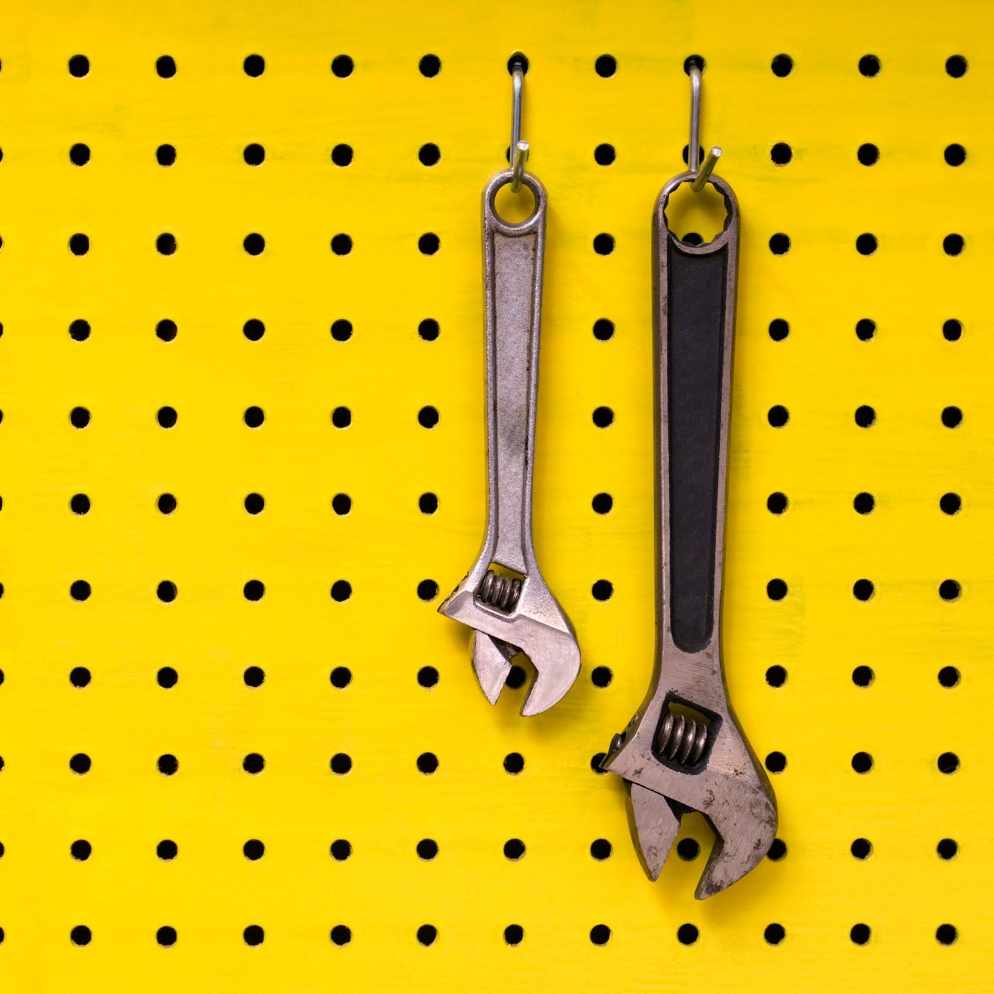Two wrenches hang from hooks on yellow pegboard