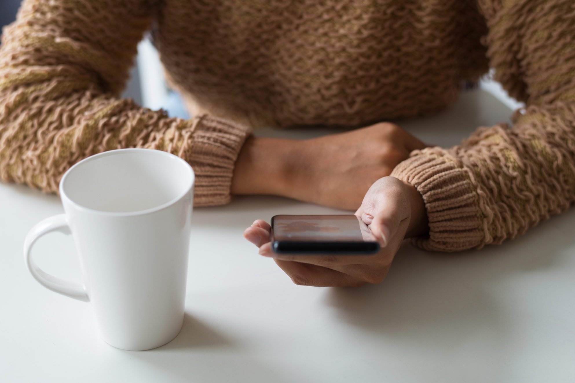 Close-up of lady in warm sweater using smartphone in office