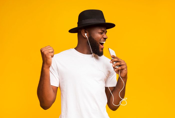 Happy african man in hat singing into smartphone like microphone