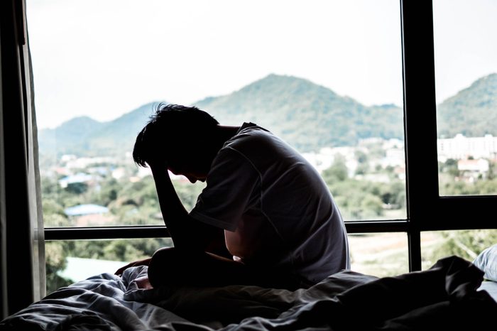 Side View Of Sad Man Sitting On Bed By Window