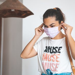 Woman putting mask on her face before leaving home
