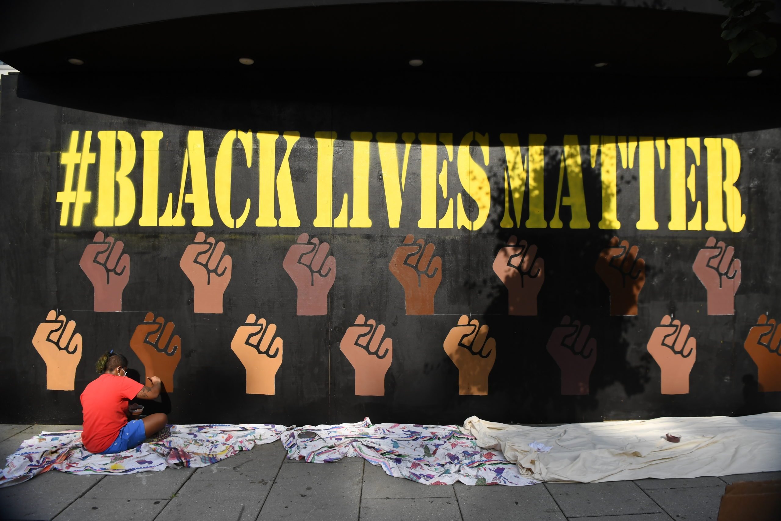 a woman works on painting a black lives matter mural in washington dc