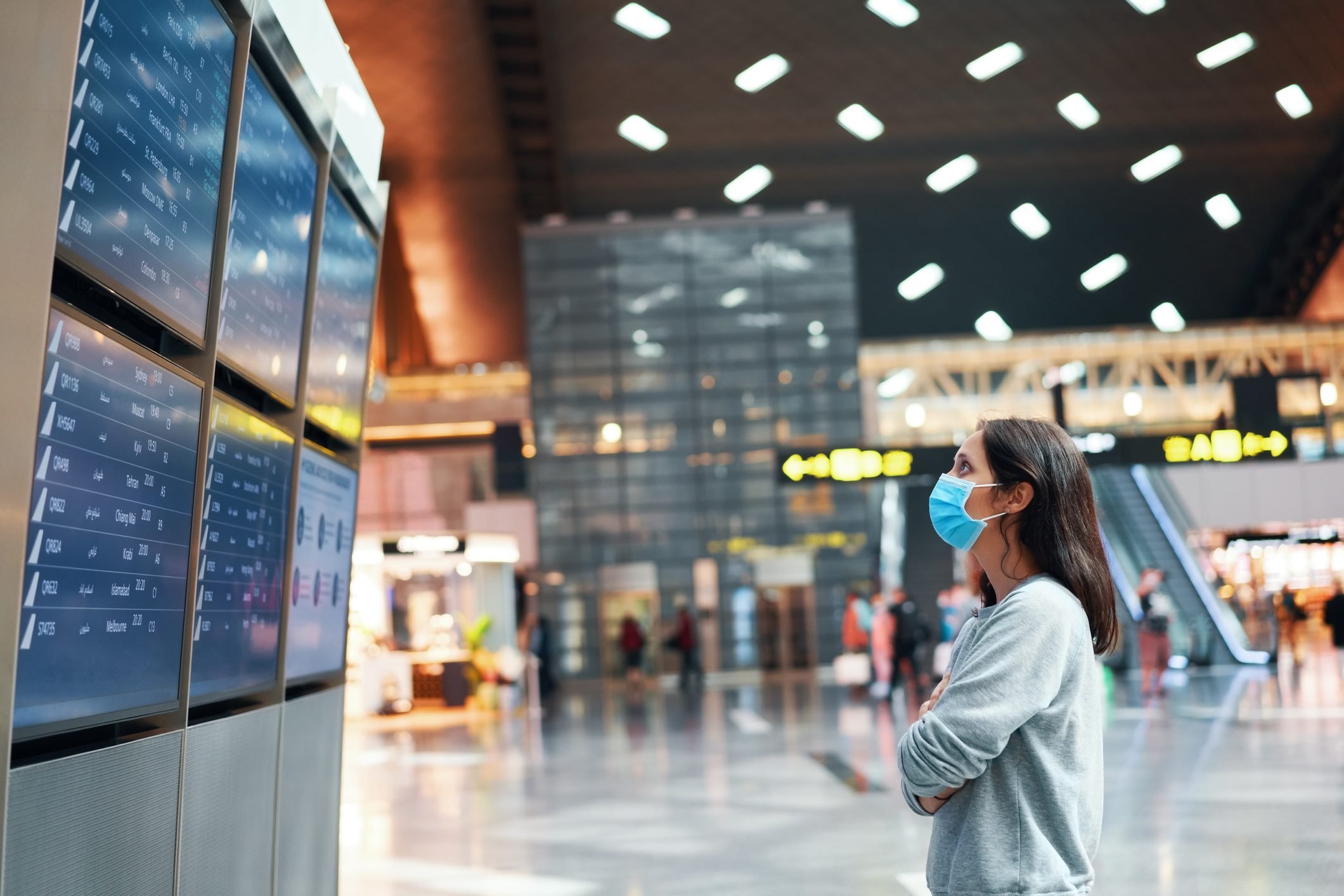 Woman in virus protection face mask looking at information board checking her flight in international airport