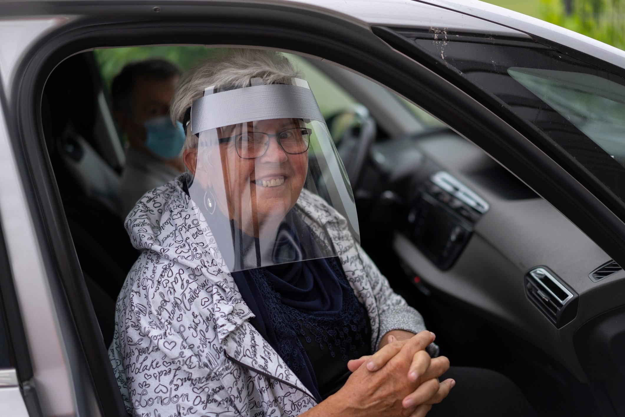 smiling elderly woman with face shield in car