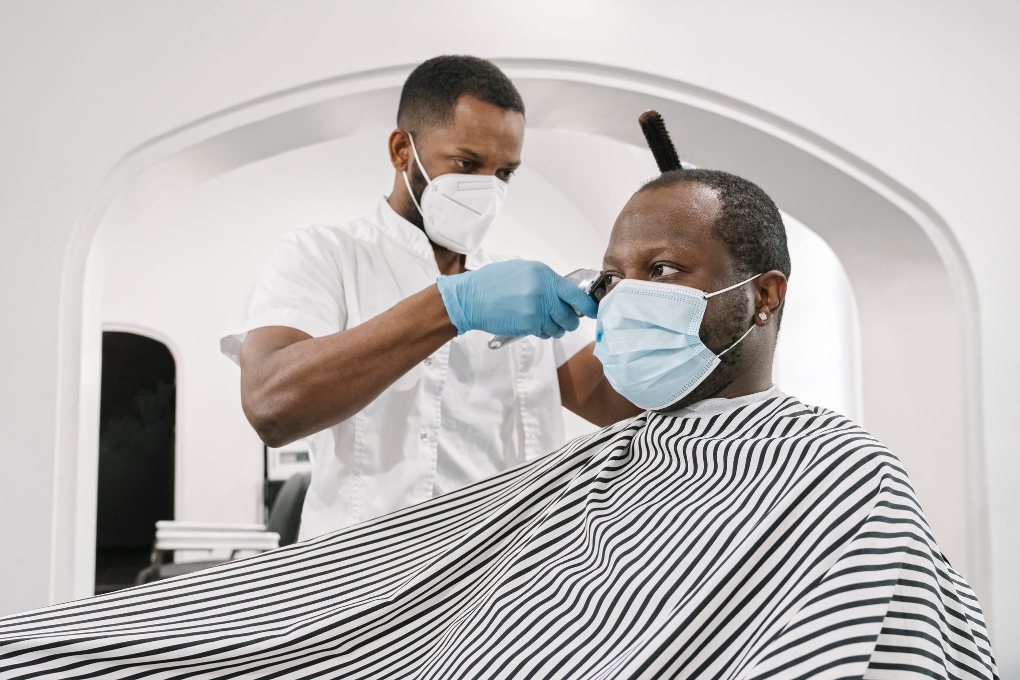Barber wearing surgical mask and gloves cutting hair of customer