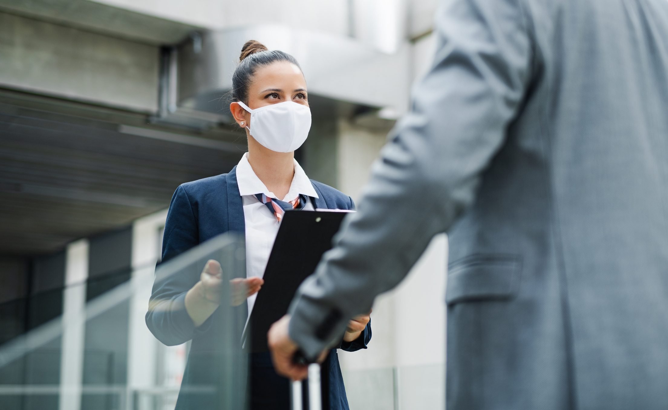 Flight attendant talking to unrecognizable businessman on airport, wearing face masks.