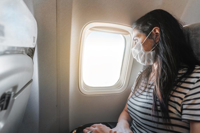 Young woman with protection mask is sitting in airplane and watching the view from window. Corona virus outbreaking.