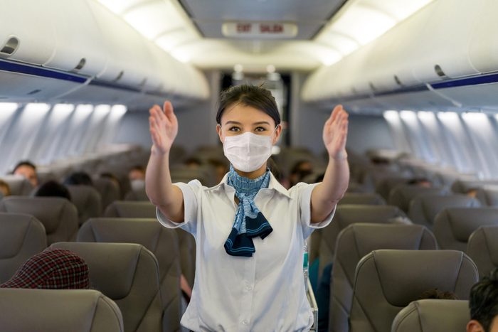 Flight attendant showing the emergency exit in an airplane wearing a facemask