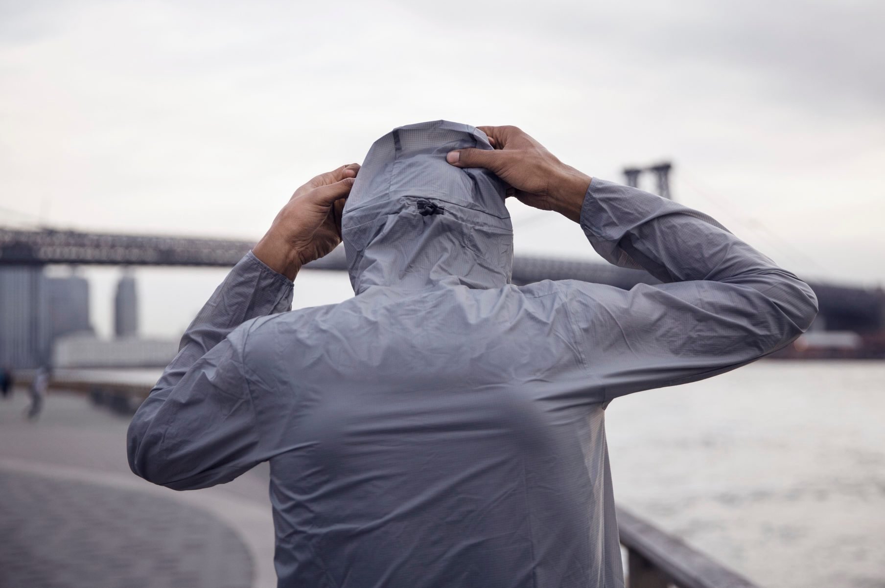 Rear view of male athlete wearing hooded jacket with Williamsburg Bridge in background
