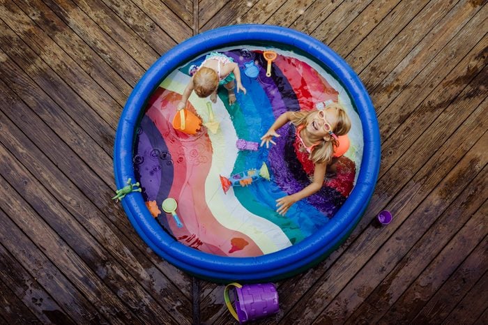 High angle view of sisters playing in wading pool on wood