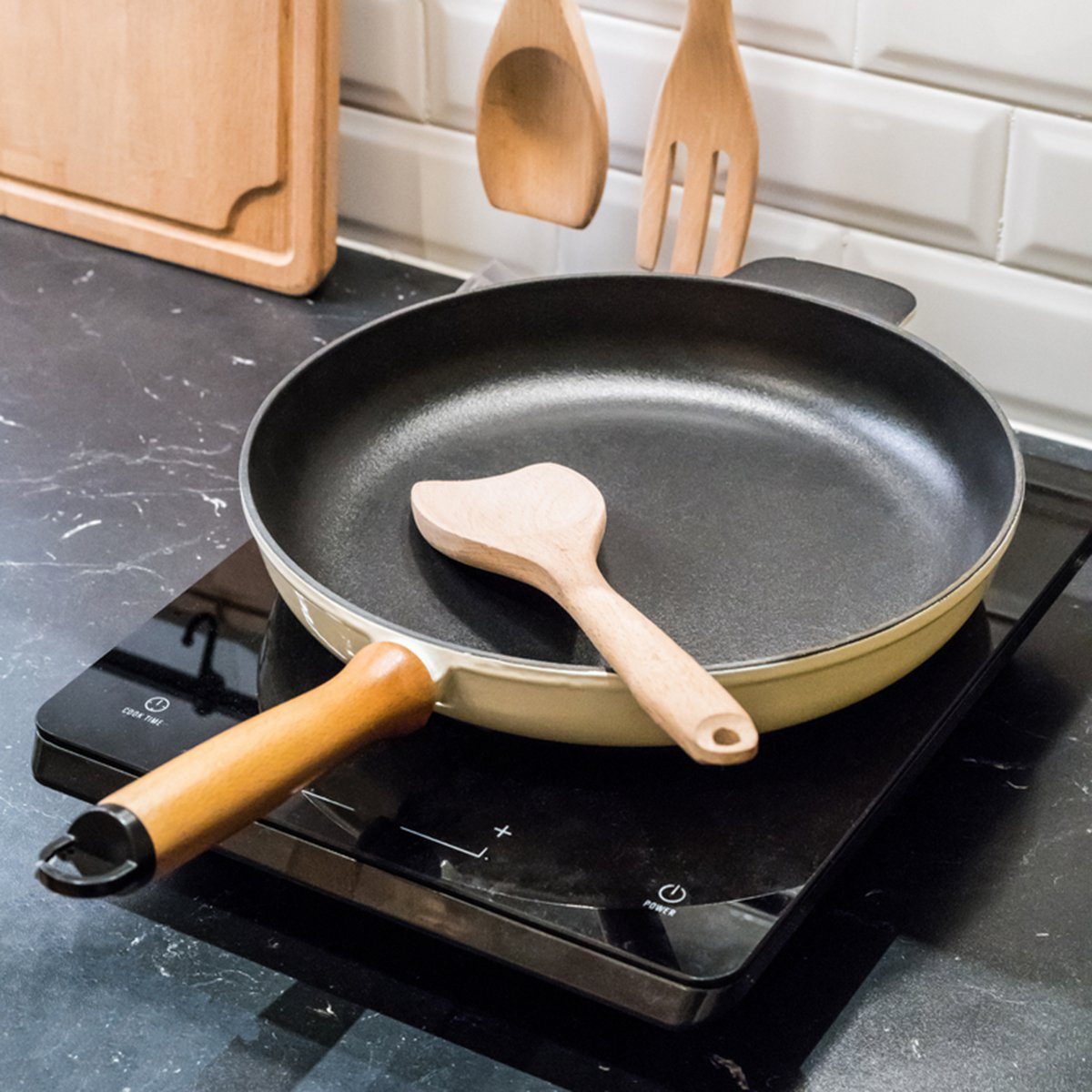 Spatula in skillet teflon coating pan on electric stove against spoon and fork hanging on white brick wall in small kitchen