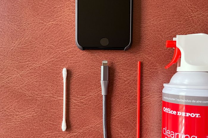 close up of iphone charging port with lightning cord and cleaning supplies; q-tip cotton swab and can of compressed air