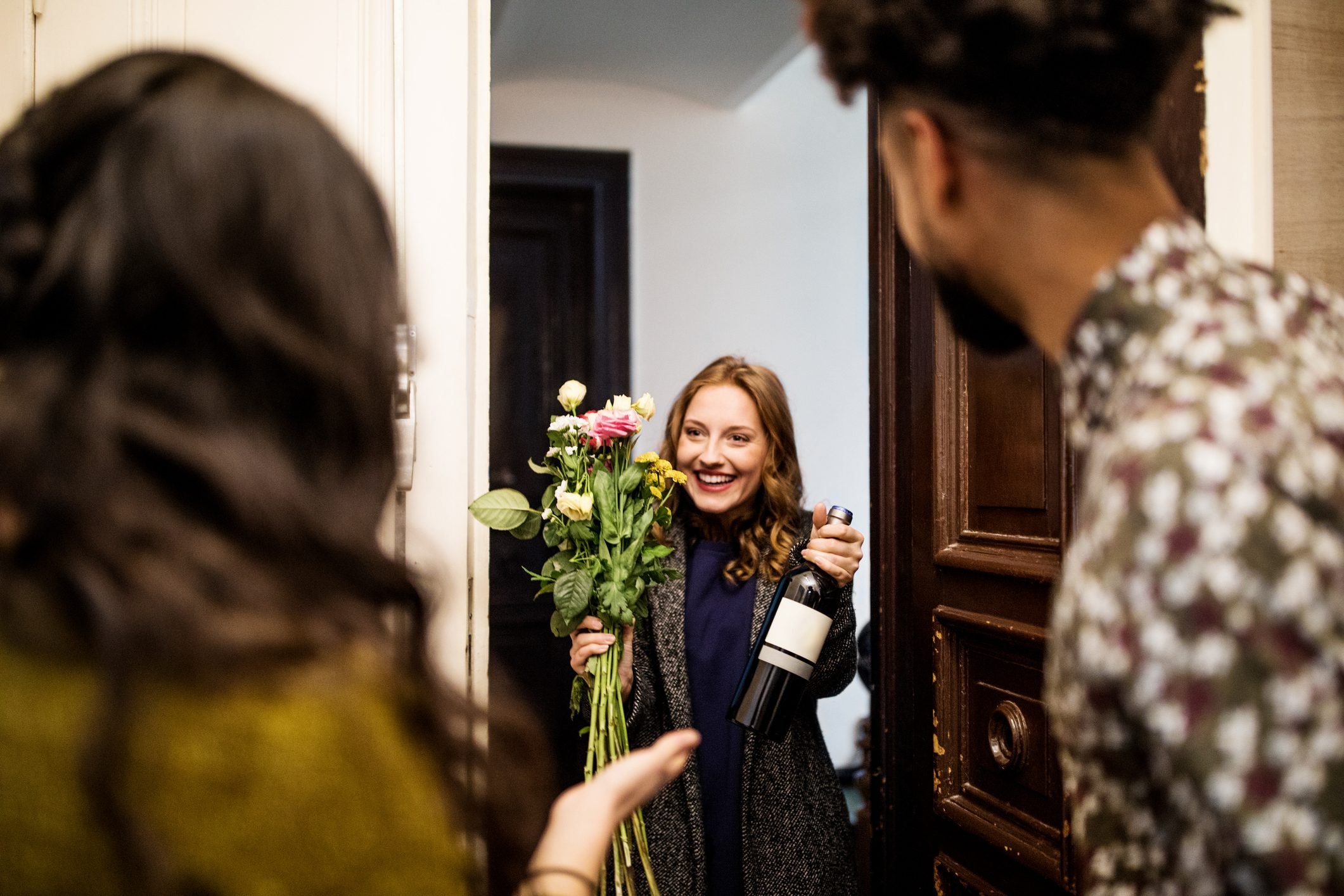 Woman holding bouquet and wine bottle while visiting friends
