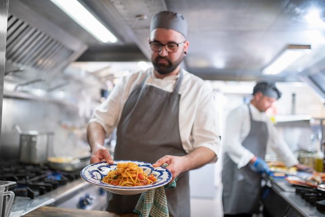 Chef presenting pasta dish in Italian restaurant kitchen