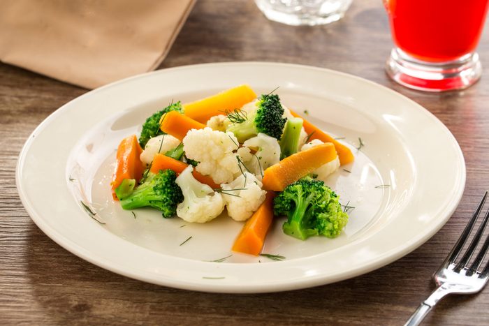Mixed vegetables cauliflower, broccoli and carrots on white plate on wooden background