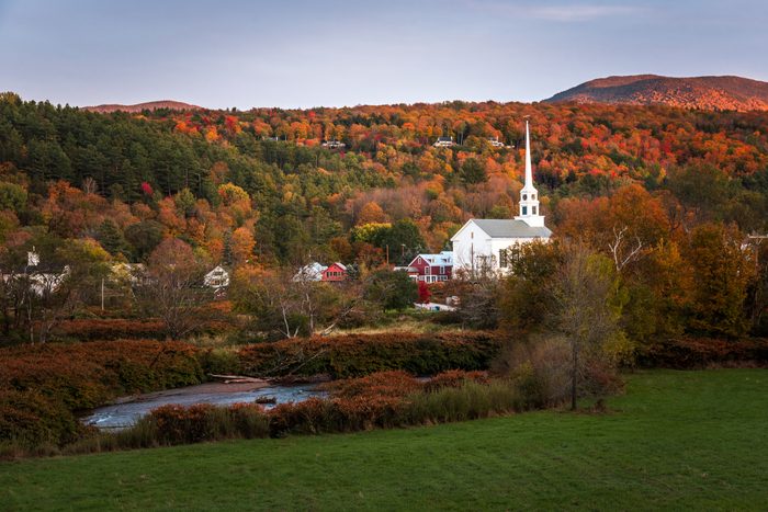Traditional white wooden church in a town surrounded by mountains covered in colourful autumnal trees at sunset
