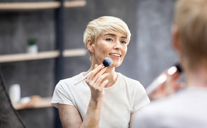 Middle-Aged Lady Using Makeup Brush Applying Bronzer Standing At Home