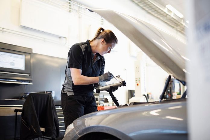 Female mechanic using technology while examining car at shop