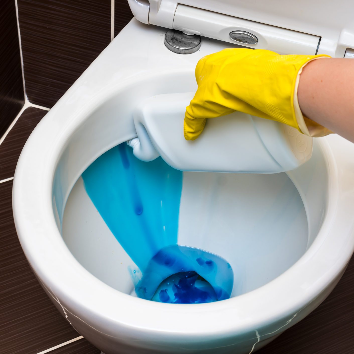Woman is cleaning toilet bowl using detergent