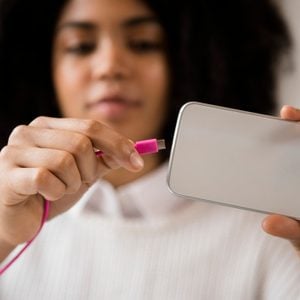African American woman connecting cable to cell phone