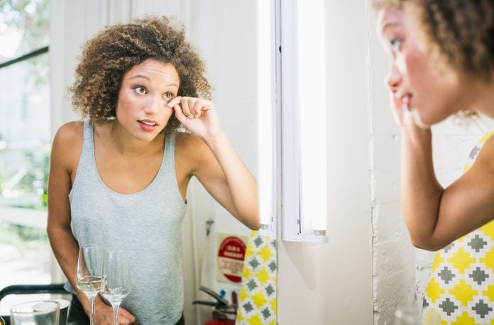 Mixed race woman doing make up in front of mirror.