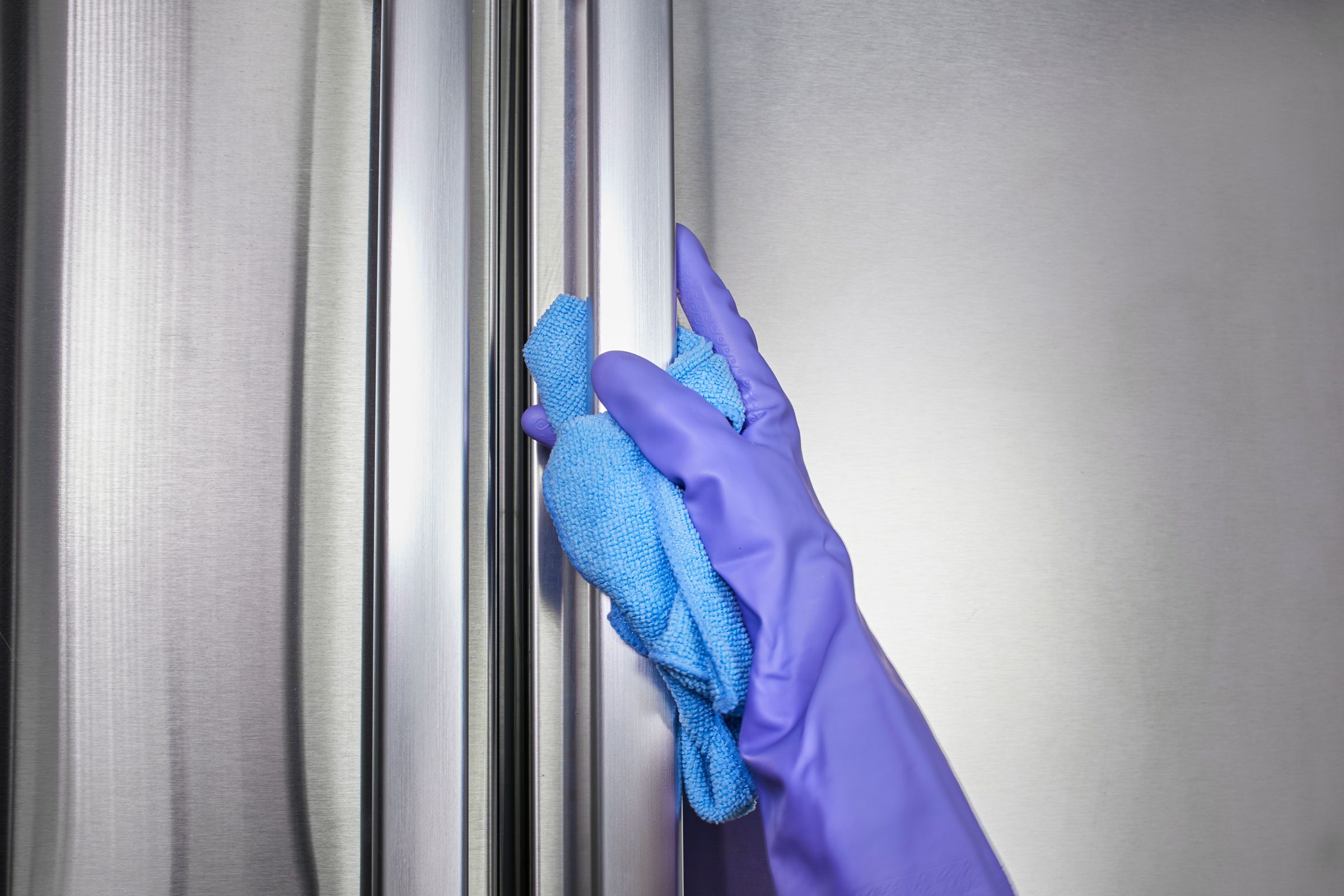 gloved hand cleaning the outside of a stainless steel refridgerator with a blue mircofiber cloth