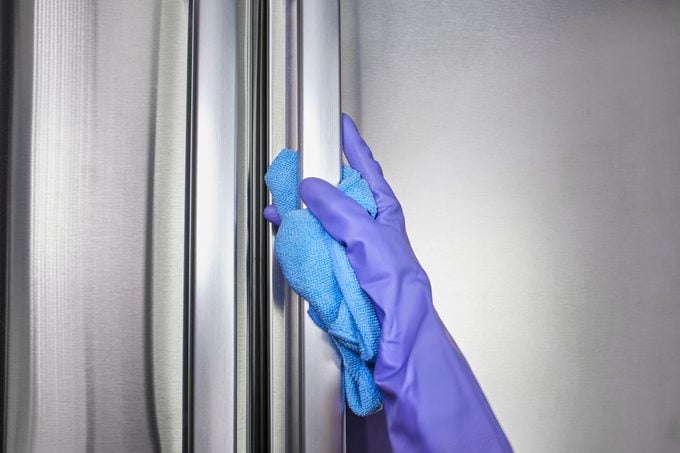 gloved hand cleaning the outside of a stainless steel refridgerator with a blue mircofiber cloth