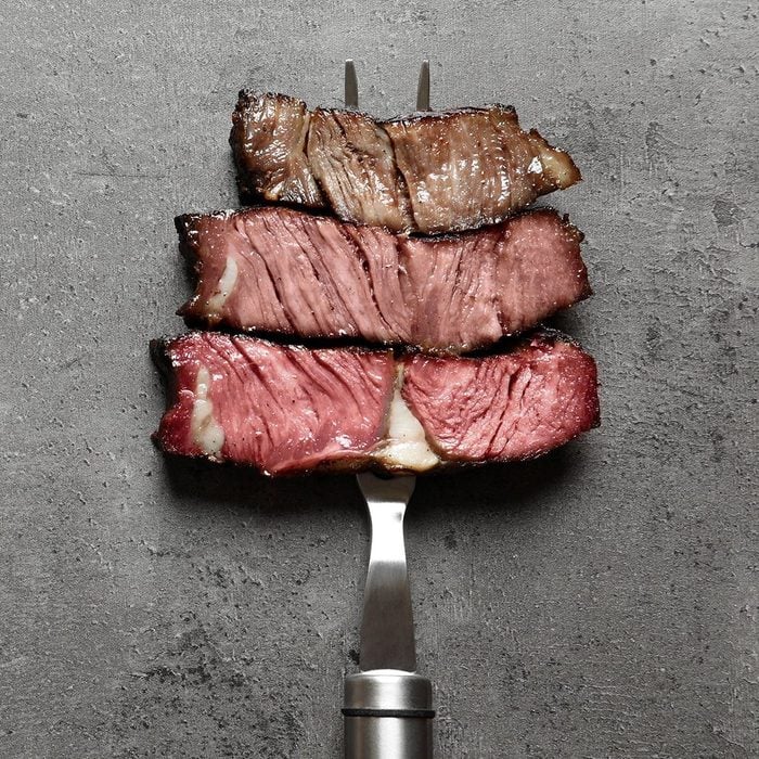 Fork with pieces of delicious barbecued meat on gray background