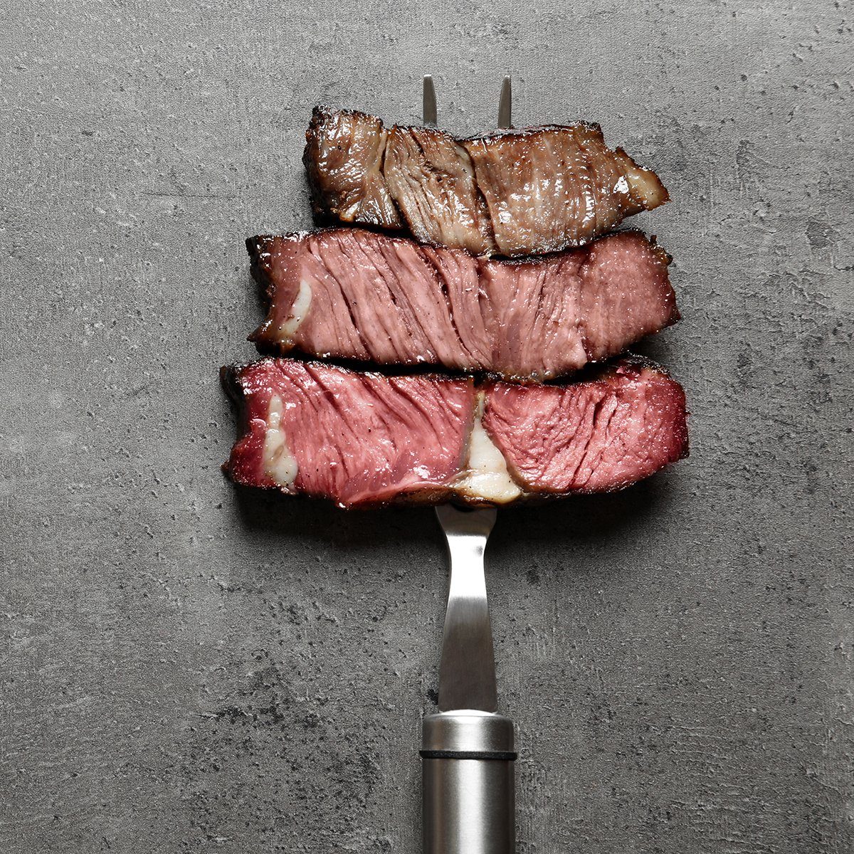 Fork with pieces of delicious barbecued meat on gray background