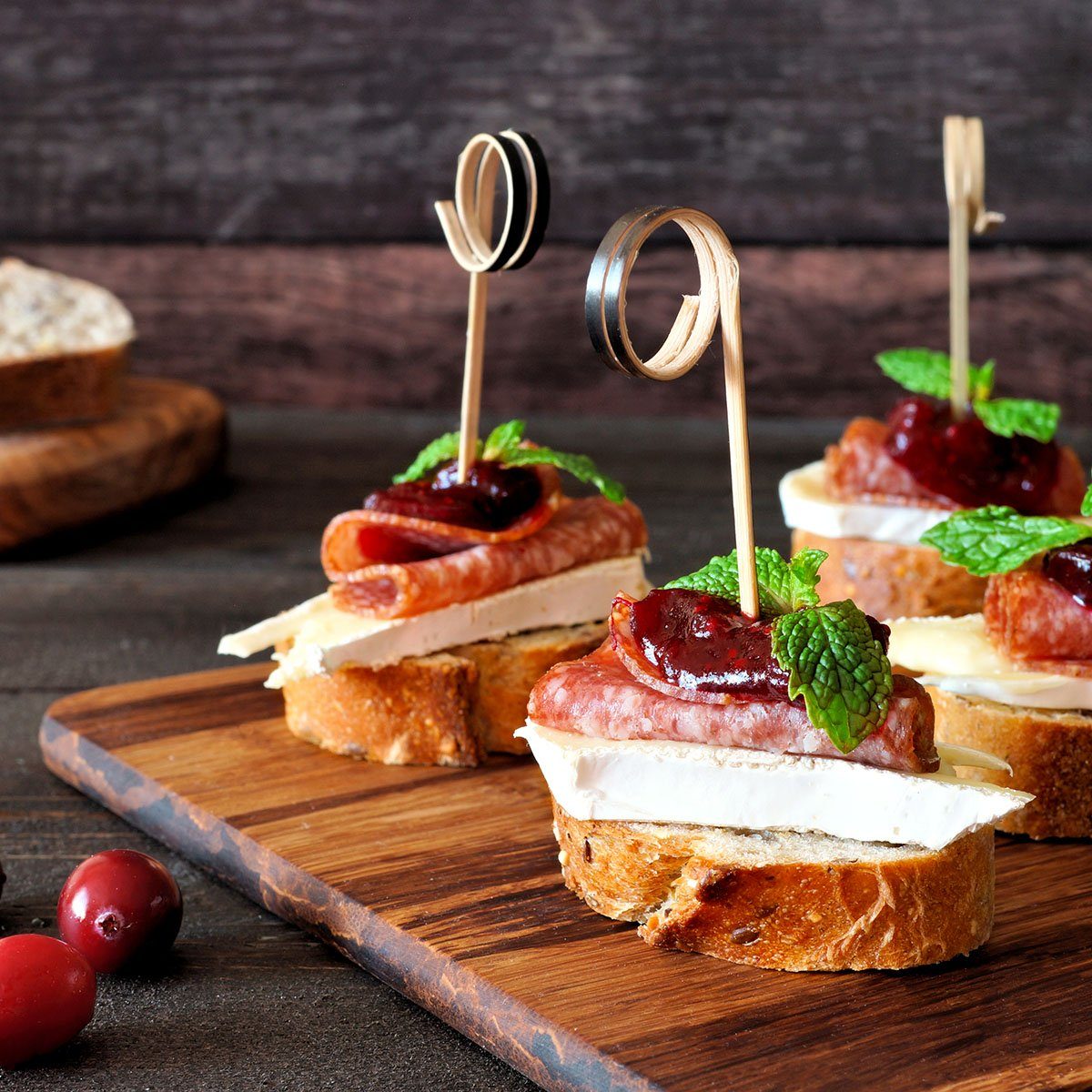 Holiday crostini skewers with cranberry sauce, brie, salami, and mint on a wooden server