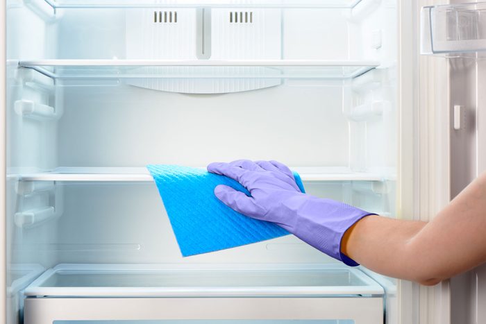 Hand In Purple Glove Cleaning empty Refrigerator With Blue microfiber cloth