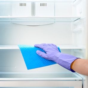 Hand In Purple Glove Cleaning empty Refrigerator With Blue microfiber cloth