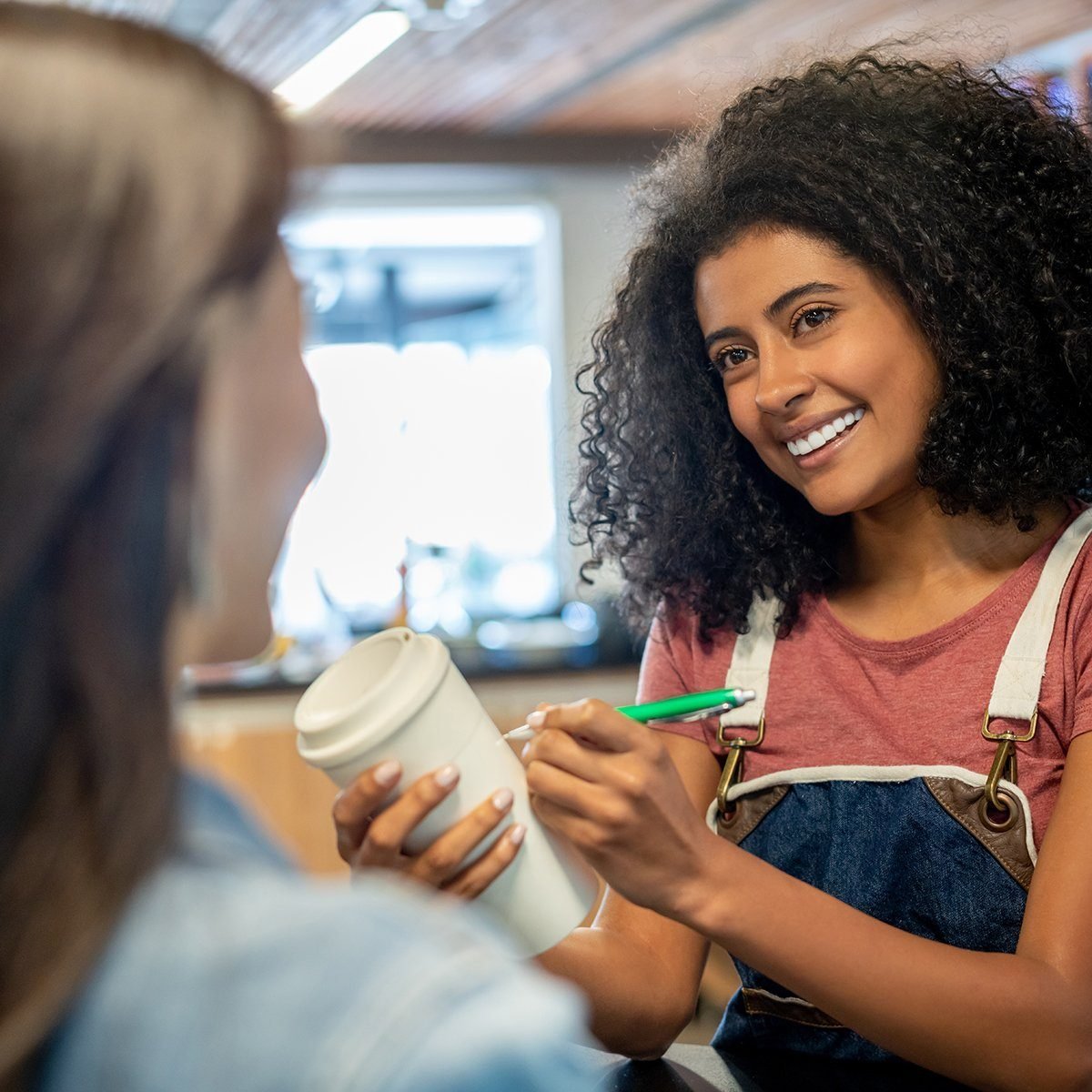 Friendly black waitress asking female customer her name to write on her coffee to go cup while smiling