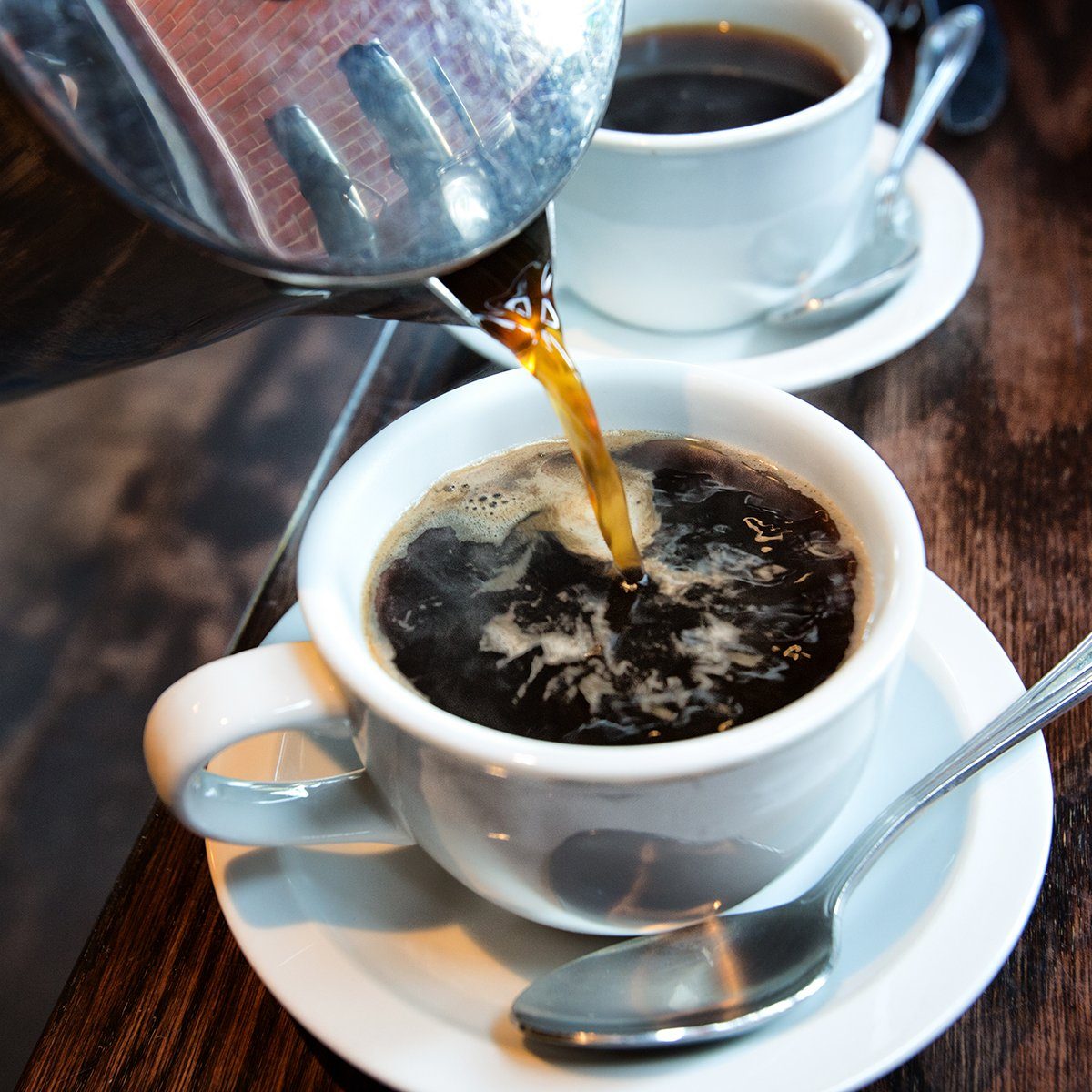 Fresh hot coffee being poured into a cup from a stainless steel french press in a trendy cafe