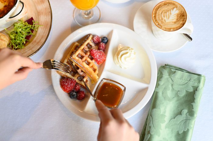 morning Breakfast or brunch in the restaurant. table with drinks and food. women's hands cut Viennese waffles with a knife and fork. selective focus