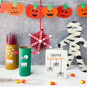 Kids Halloween Crafts arranged on a simple background; jack-o-lantern garland, toilet paper roll monsters, yarn and popsicle stick spider web, thumbprint spider card, masking tape mummy